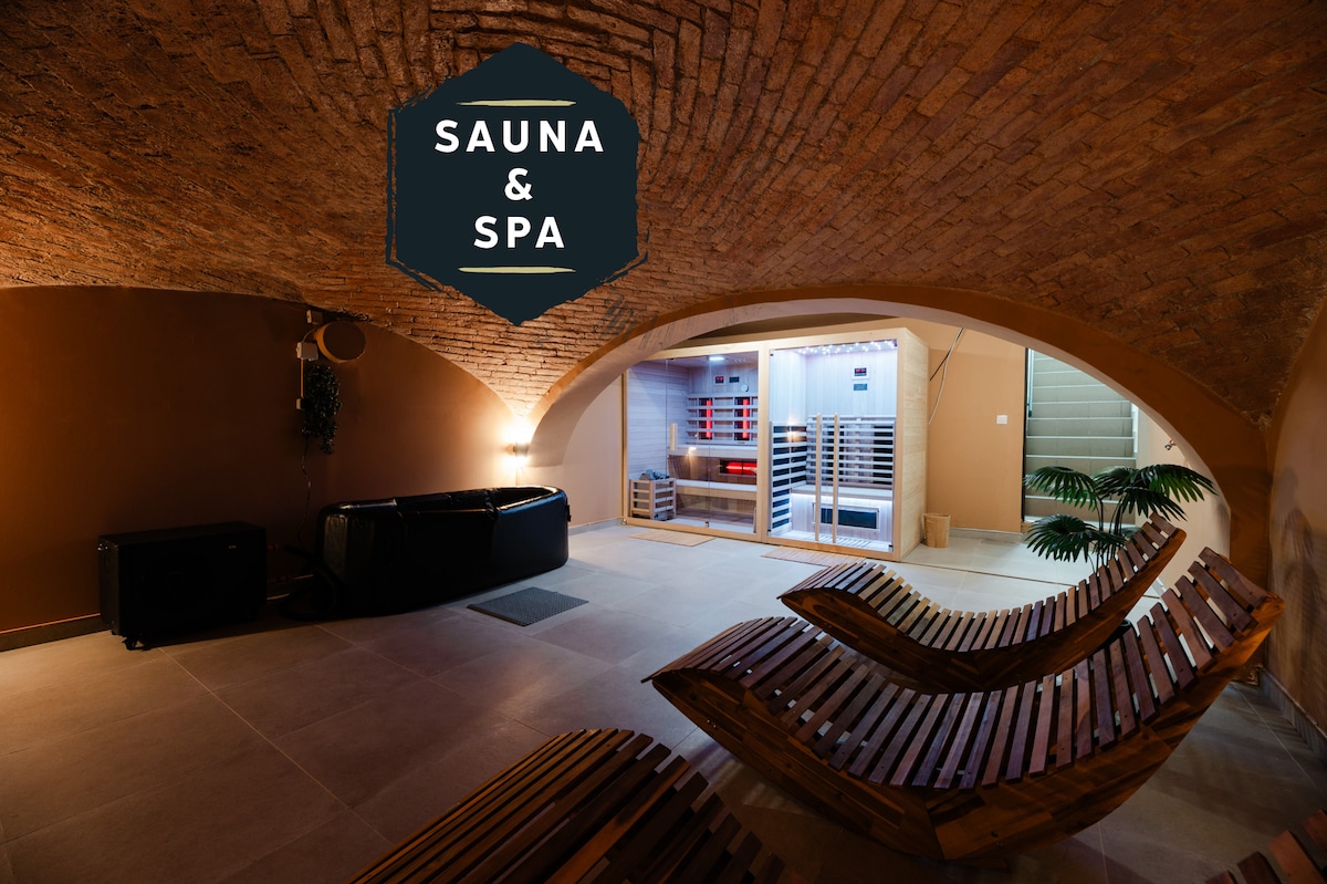 The wellness area features a sauna surrounded by modern wooden loungers, complemented by a subtly lit space with rustic brick arches. A hint of greenery is visible, enhancing a serene environment for relaxation.