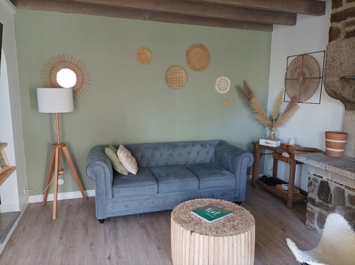 The living area features a plush blue couch with tufted detailing, complemented by a round wooden coffee table. A floor lamp stands beside the couch, and wall decor includes circular woven art. Natural light illuminates the space, enhancing the earthy tones.
