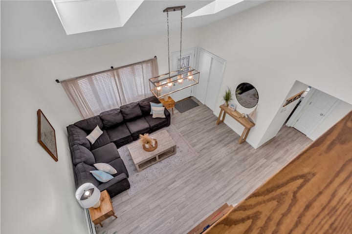 **Bright and Inviting Living Room**  
This airy living room features skylights, a vaulted ceiling, and a cozy sectional perfect for relaxing. The warm, modern decor and natural light create a welcoming space to unwind after a day of adventure.