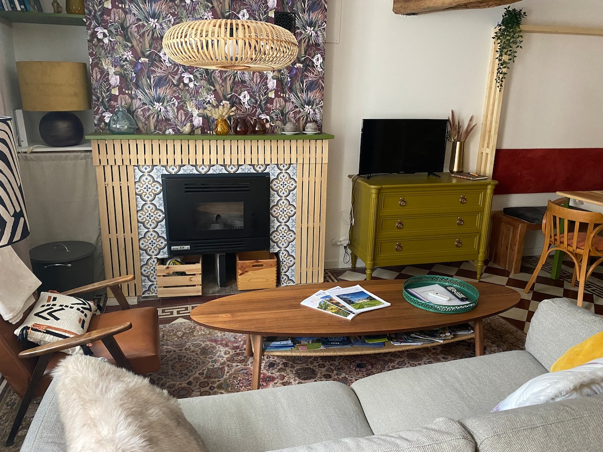 A bright living area features a stylish coffee table in front of a modern fireplace, surrounded by colorful decor. Textured wallpaper with a natural motif adds depth, while a flat-screen TV sits on a side cabinet. A cozy sofa provides comfortable seating.