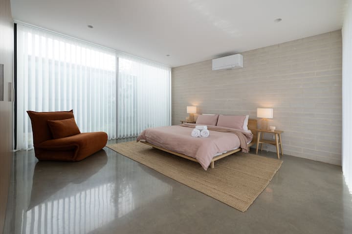 The fourth bedroom offers a queen bed with soft linen, sheer curtains and electric block out blinds. A view of the internal courtyard and access to the private backyard.