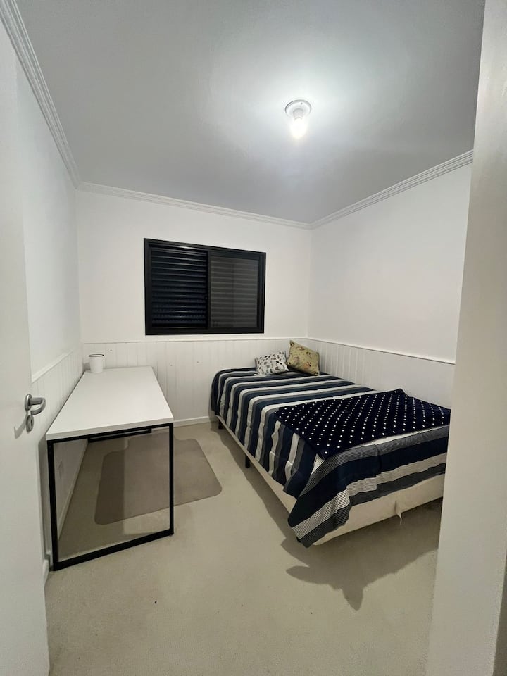 חדר שינה מרווח עם פינת עבודה. מיטה זוגית קטנה ושולחן מרווח. יש בו ארון עם כמה קולבים, מגירות ושפע של מקום.