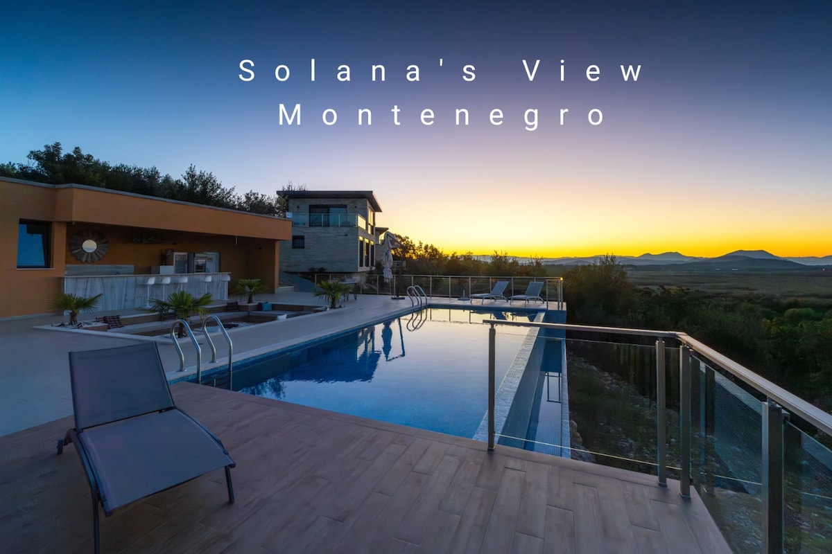 A modern structure is positioned beside a tranquil infinity pool, reflecting the evening sky's hues. The outdoor area includes a lounge space with stylish seating. Surrounding hills create a serene backdrop, enhancing the peaceful atmosphere of the vacation homes.