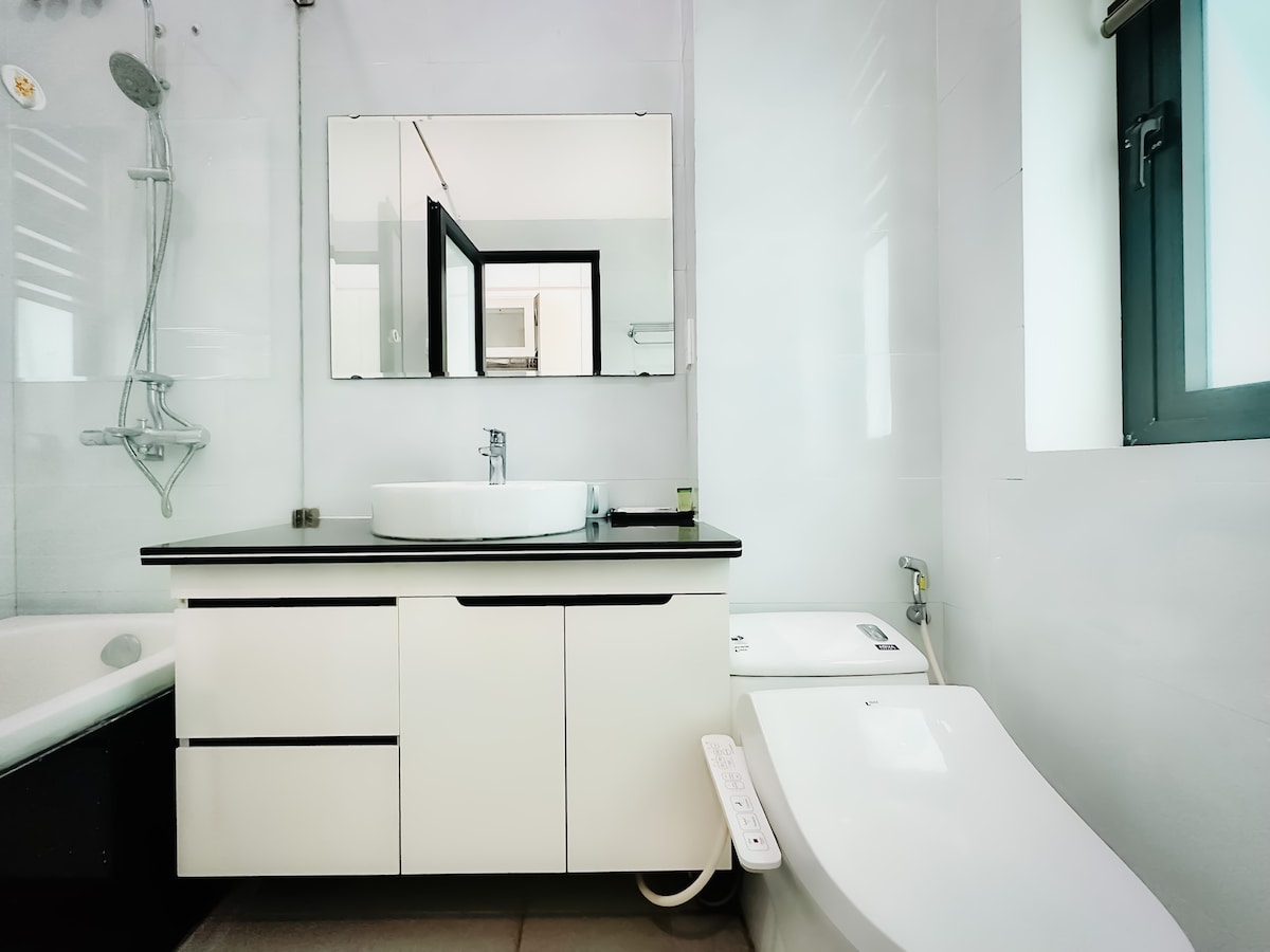 A modern bathroom is displayed, featuring a sleek white sink atop a minimalist black countertop. A large mirror reflects the space, while a stylish shower area is visible. A contemporary toilet is positioned beside a spacious bathtub, providing functional elegance.
