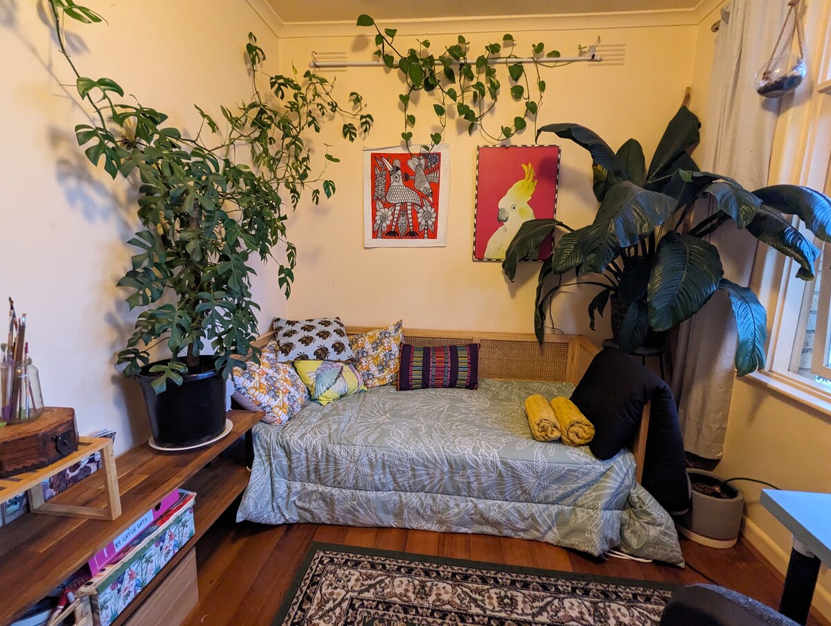 Një krevat tek me shumë batanije, bimë dhe jastëkë. 