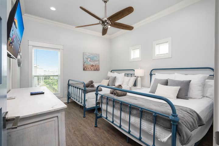 ผ่อนคลายในห้องนอนที่มีเตียงควีนไซส์ 2 เตียงและเพลิดเพลินกับทีวีจอแบน Roku โต๊ะข้างเตียงมีโคมไฟแบบสัมผัสพร้อมพอร์ตชาร์จ และตู้ใต้ทีวีมีเกมกระดานเพื่อเพิ่มความสนุกสนาน