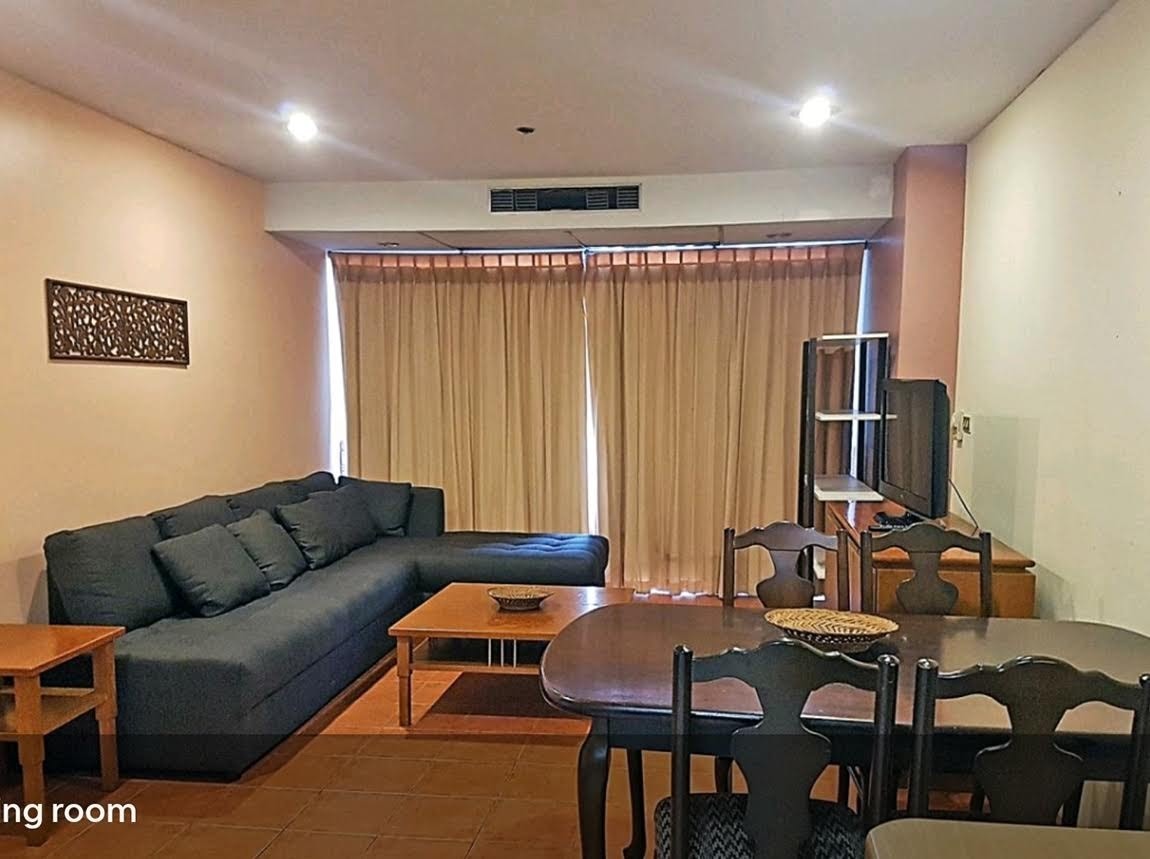 A spacious living room area features a large sectional sofa and a wooden dining table. Natural light is welcomed through floor-to-ceiling windows adorned with sheer curtains, while a television is positioned nearby for entertainment.