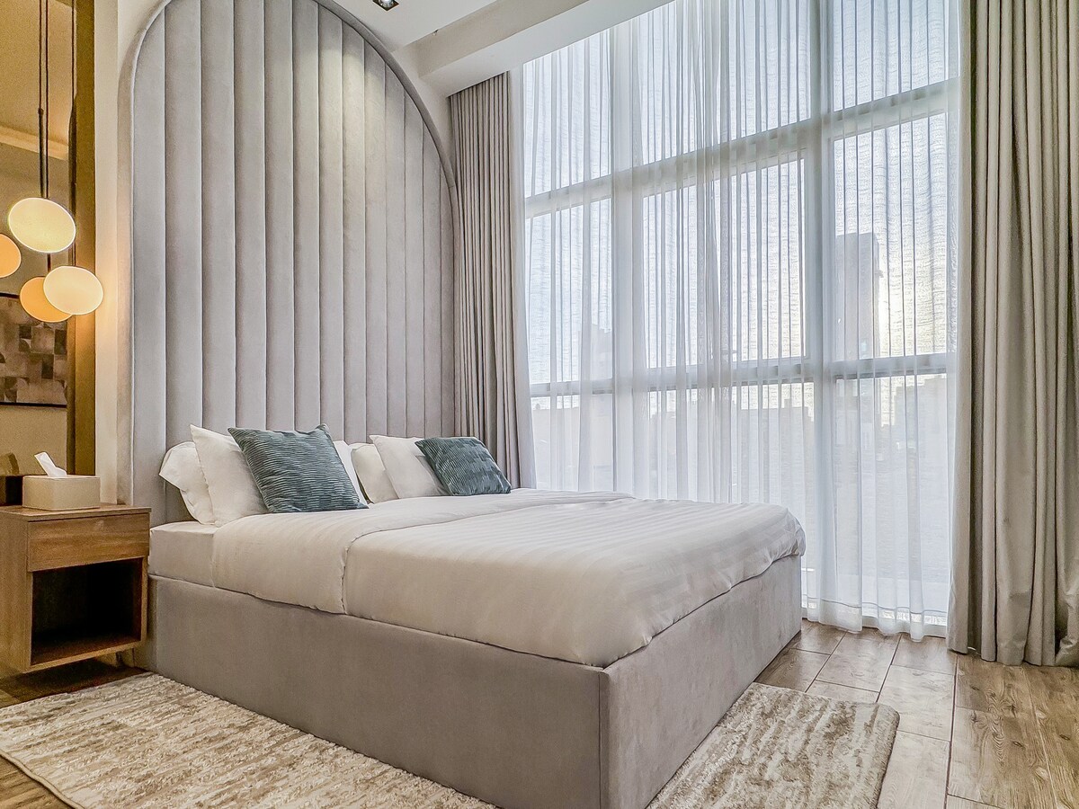 ห้องนอนพร้อมเตียงคิงไซส์และหน้าต่างสูงจากพื้นจรดเพดานมองเห็นถนนคิงฟาฮัด
