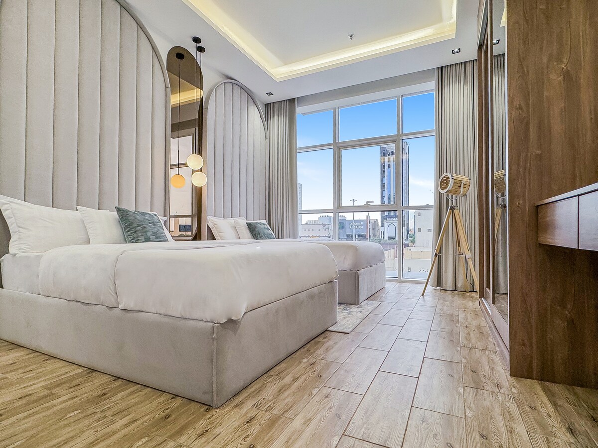 ห้องนอนในตัวกว้างขวางพร้อมเตียงควีนไซส์ 2 เตียงและหน้าต่างสูงจากพื้นจรดเพดานมองเห็นถนนคิงฟาฮัด
