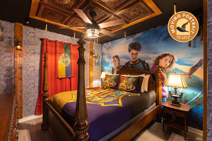 היכנסו לעולם הקסמים עם חדר השינה בהשראת הארי פוטר! מיטת אפיריון מלכותית עם מצעים של בית הוגוורטס ניצבת מול ציור קיר של דיוקן זז של הארי, רון והרמיוני. אריחי תקרה קסומים, נרות צפים             