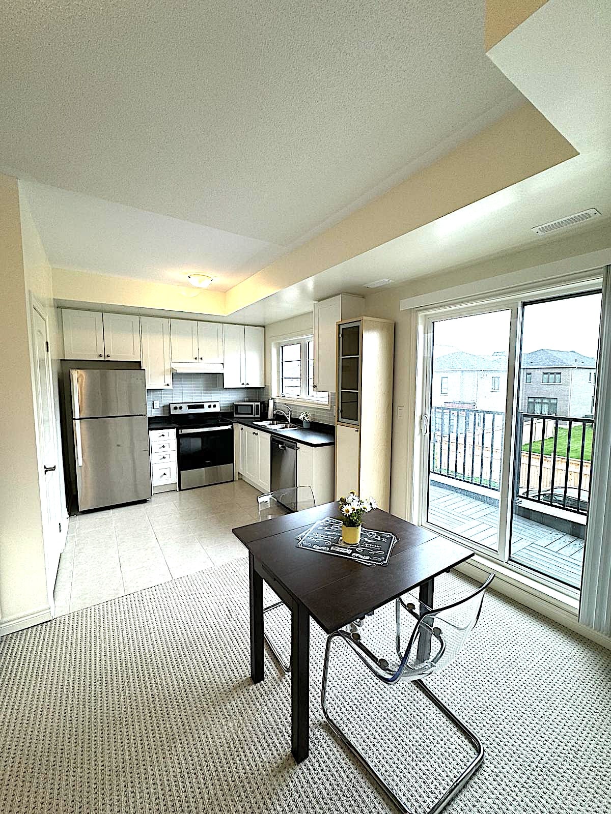 The kitchen and dining area feature modern appliances in a sleek design. A metal dining table is complemented by a chair, while a small vase with fresh flowers adds a touch of elegance. Natural light floods the space through the large sliding glass door, opening to the private balcony.