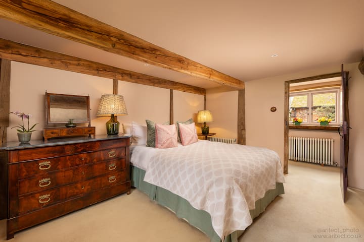 Quarto de hóspedes 1 no térreo com fácil acesso ao banheiro, cama king size, cômoda e guarda-roupa pendurado.