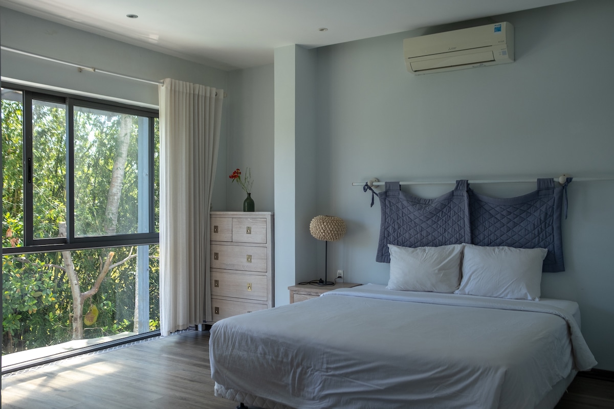 Un lado del dormitorio con una cama doble tamaño king, almacenamiento y grandes ventanales