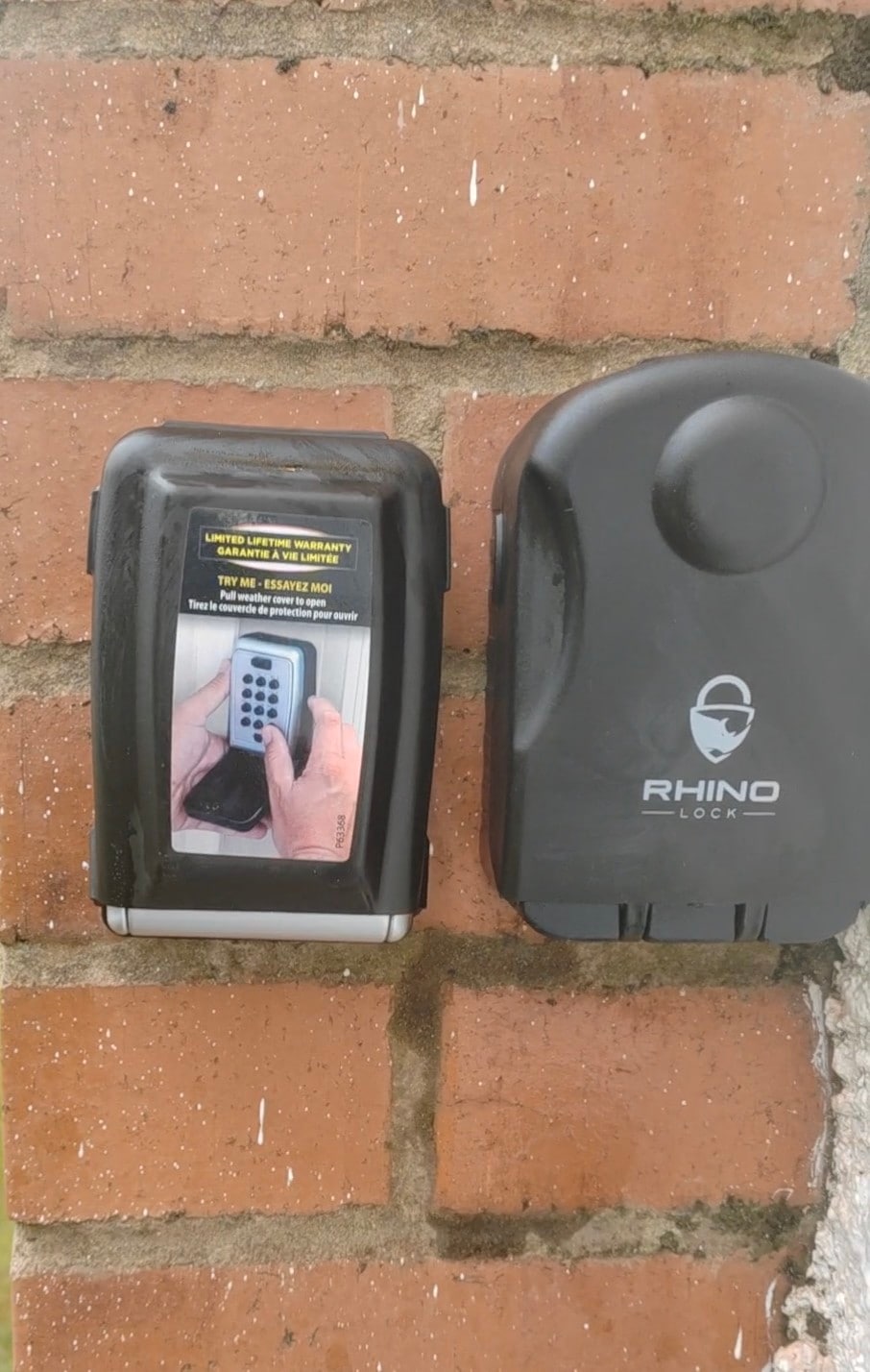 A key safe is mounted on a brick wall, designed for secure access. The key safe features a visible keypad and a transparent section displaying instructions for use. The adjacent compartment, labeled with a logo, serves as the locking mechanism, contributing to the overall security of the entrance.