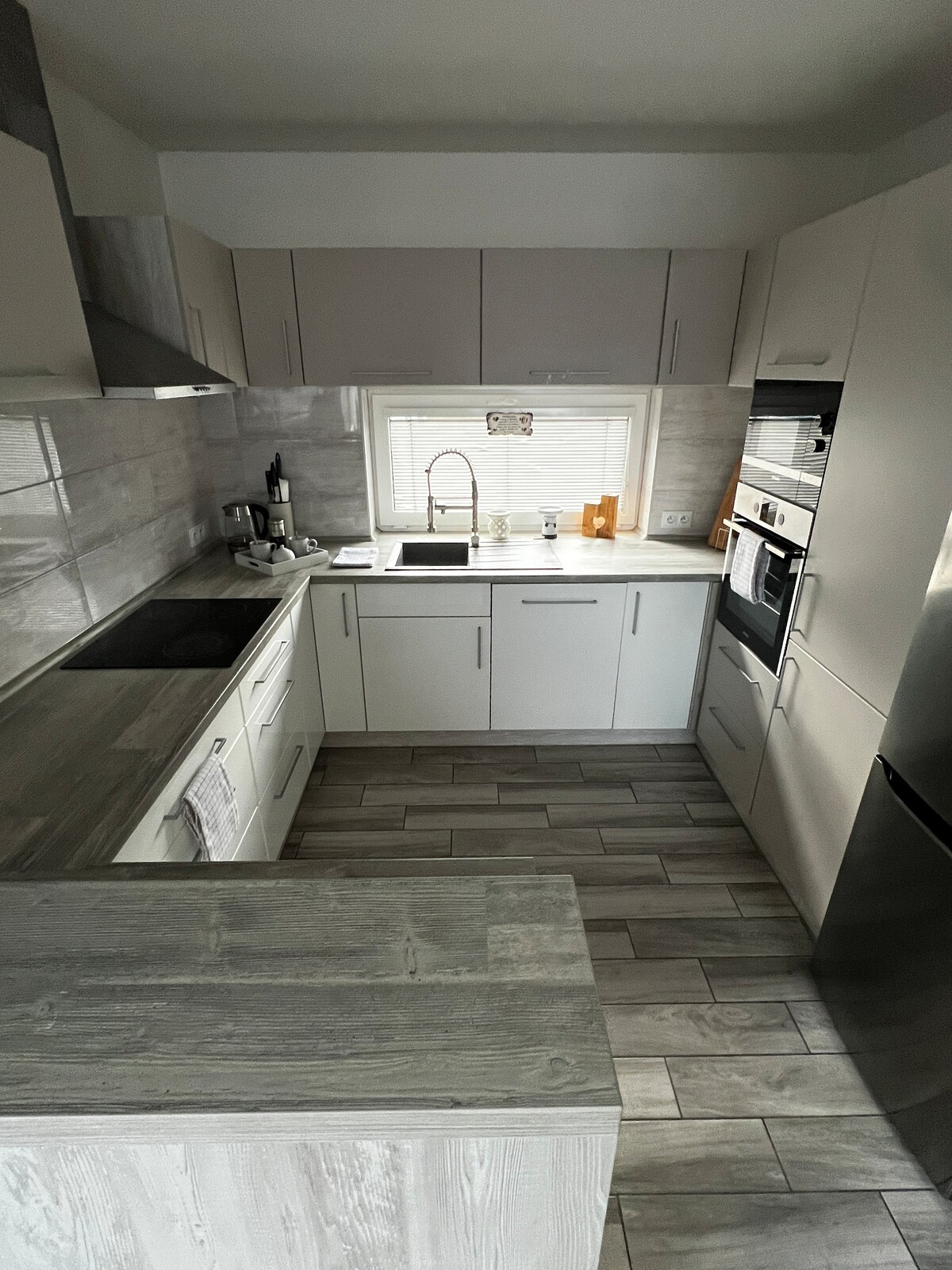 The kitchen features modern cabinetry and a functional layout. A sink is positioned below the window, providing natural light. Essential appliances, including a stove and refrigerator, are neatly integrated, showcasing a clean and inviting cooking space.