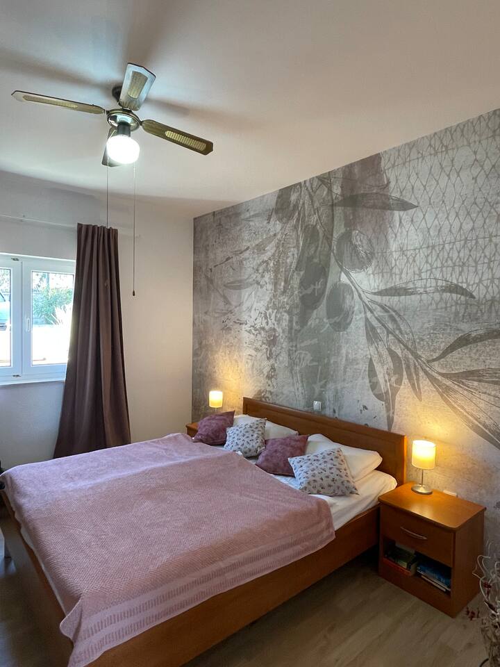 Spavaća soba s bračnim krevetom i motivom dalmatinskog stabla na zidu