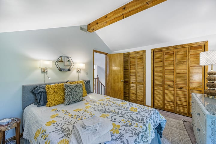 Second-floor queen bedroom with bright floral decor, vaulted ceilings, and cozy touches for a restful retreat.