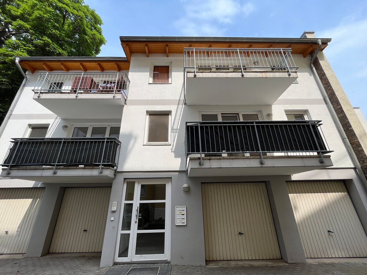 The building features a clean, modern facade with two levels of balconies overlooking a paved outdoor area. Large windows provide natural light, and garage doors line the ground level, accentuating the urban atmosphere of the location.