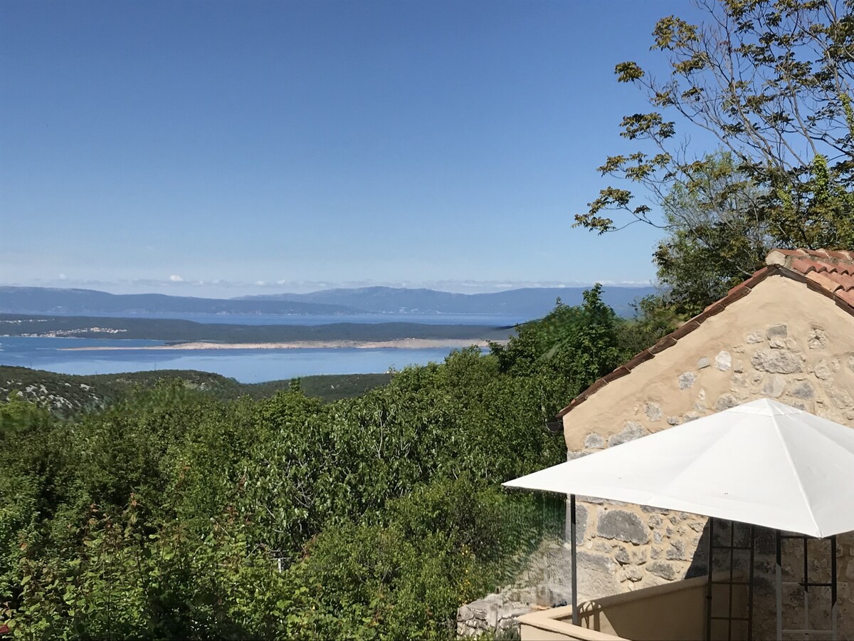 A scenic view from the villa showcases the expansive Kvarner Bay with distant islands. Lush greenery surrounds the property, complementing the tranquil atmosphere. The image captures a white parasol providing shade on the terrace, emphasizing the peaceful outdoor space enjoyed by the serene landscape.