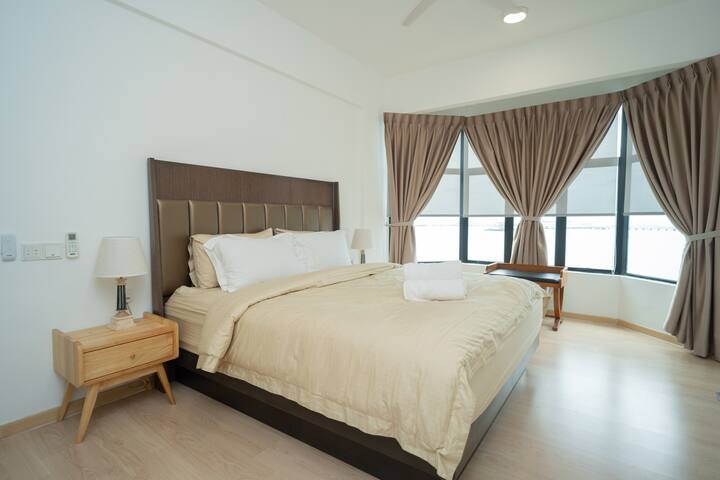 Spacious Bedroom 1 with a luxurious king-sized bed, cozy beige bedding, and plush pillows. Surrounded by large windows with blackout curtains, it’s the perfect blend of brightness and privacy for a restful stay.