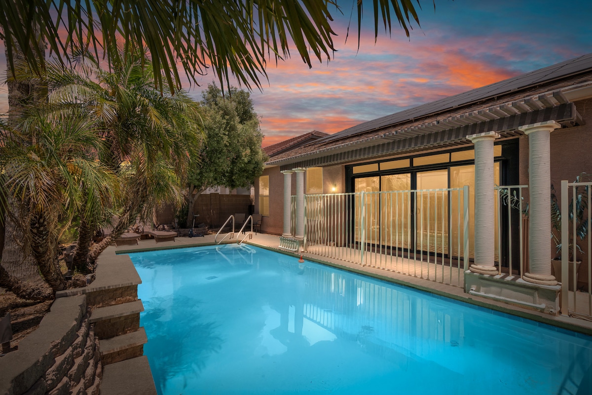 A private pool glistens under the evening sky, surrounded by palm trees and lush greenery. The tranquil water reflects the colorful sunset, while elegant columns frame the entrance to the home. Safe access is provided by a gated area, enhancing the serene atmosphere.