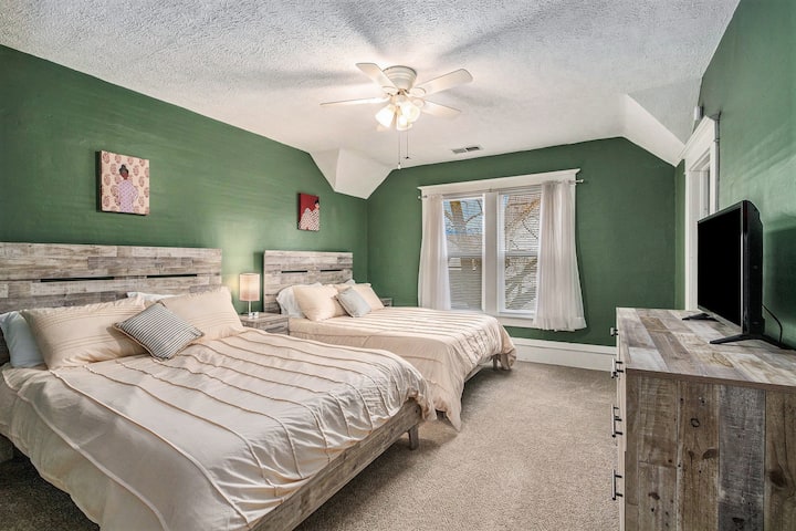 Este acogedor dormitorio con paredes verdes terrosas, con dos lujosos colchones de tamaño completo, alfombras suaves, una cómoda y un televisor de alta definición.