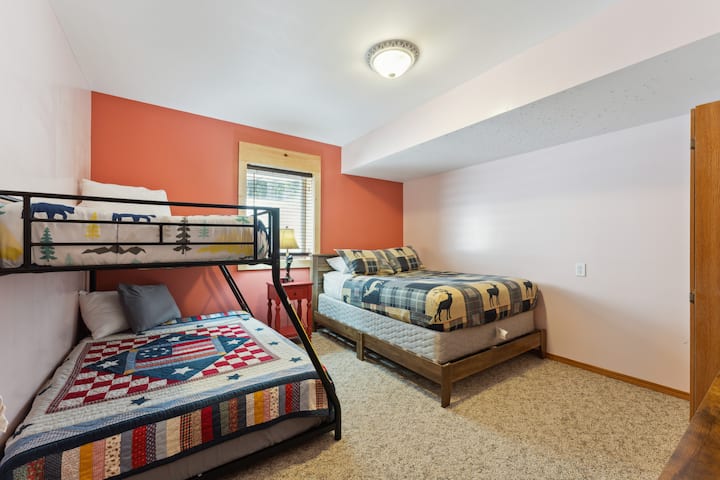 Basement bedroom with one queen bed, one bunk bed with full bed on the bottom and twin on top, dresser, Roku TV, USB charging ports, alarm clock, hangers, and closet