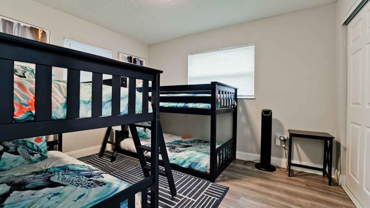 عرض من الباب. سريران بطابقين مع مكتب عمل صغير.