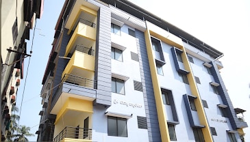 A modern multi-story building is displayed, featuring a mix of light and dark exterior panels. Large windows are visible, allowing natural light to enter the structured spaces. Balconies are present on each level, contributing to the overall contemporary design.