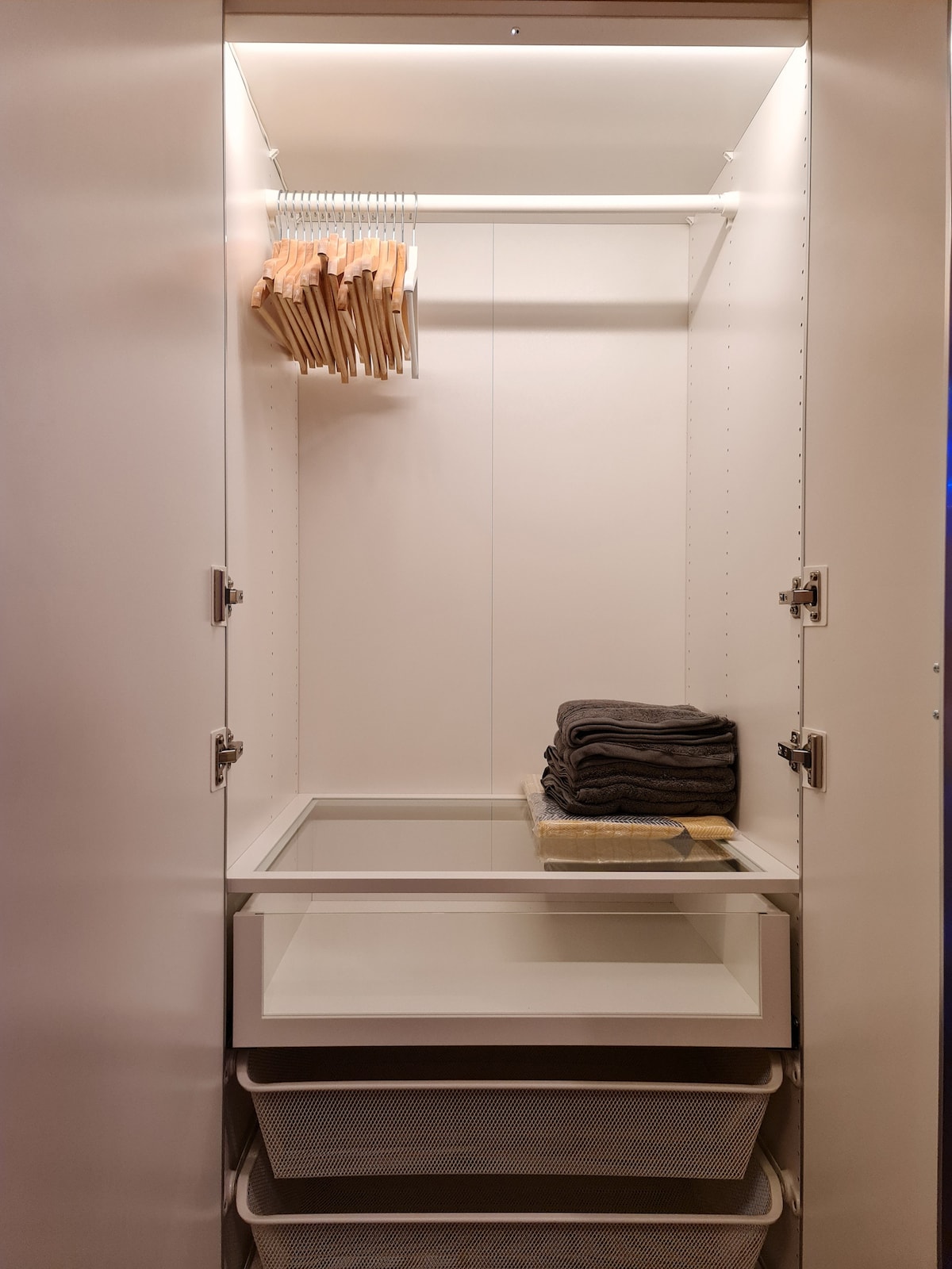 An organized closet is displayed, featuring a rod with several wooden hangers. A stack of neatly folded dark towels is placed on a shelf, while two storage drawers are visible at the bottom, offering additional space for personal items.