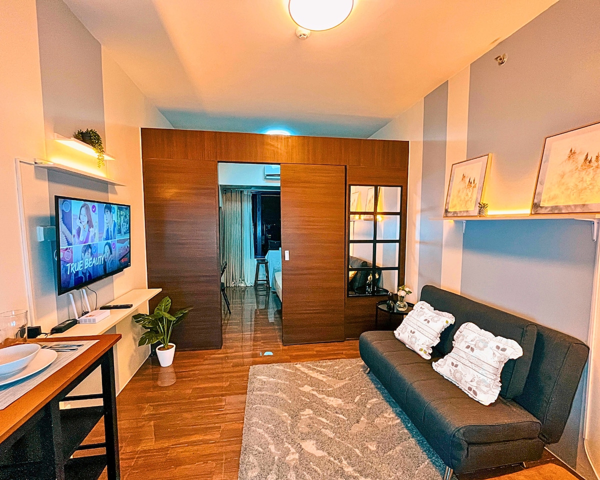 Un espacio de estar elegante y acogedor con un moderno sofá de 2 plazas que se convierte en una cama doble extraíble, un televisor inteligente con Netflix y wifi de alta velocidad. La iluminación cálida y la decoración elegante crean el lugar perfecto para relajarse, cenar o trabajar.