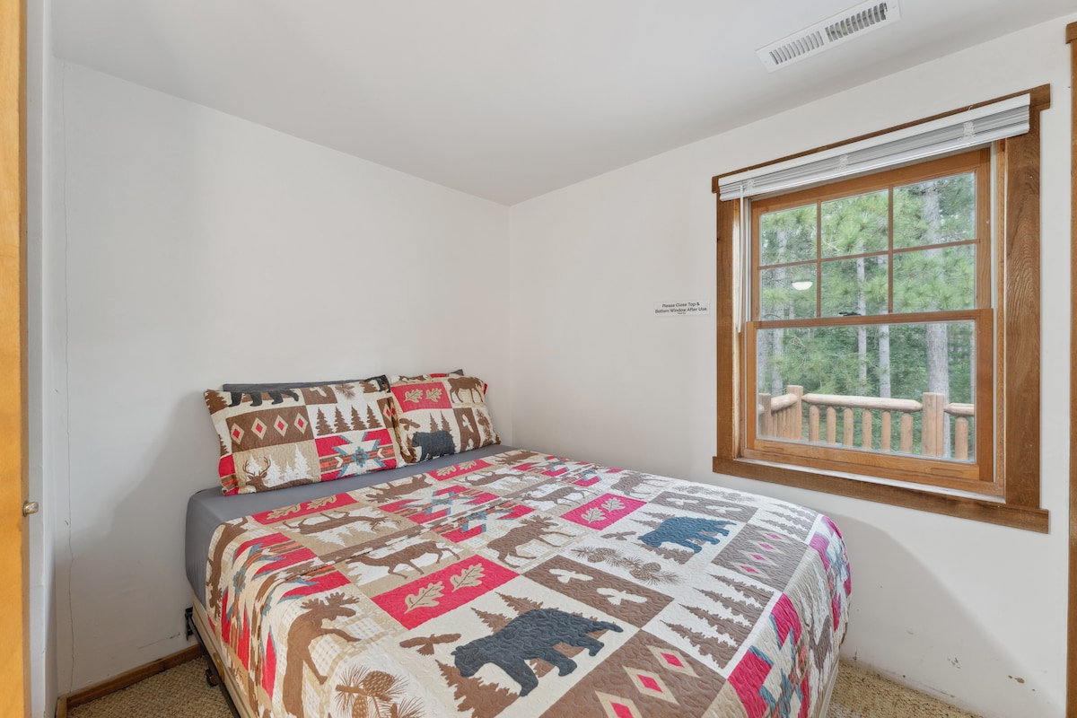 La cama completa de la cabaña de arriba incluye TV Roku, cómoda, despertador con cargador USB, ventilador portátil, almohada y mantas adicionales, armario con perchas y acceso al balcón.