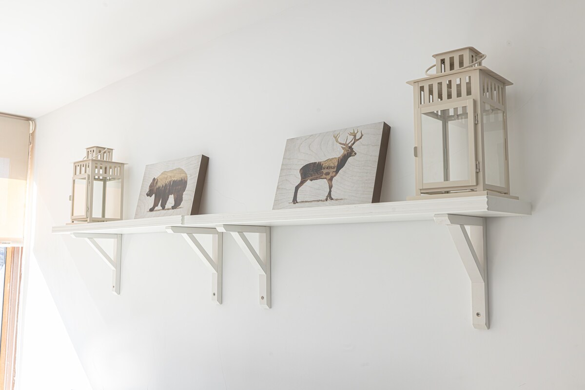 A white shelf is mounted on a light-colored wall, displaying two decorative lanterns and three framed art pieces featuring wildlife motifs. The arrangement adds a touch of natural elegance to the space.