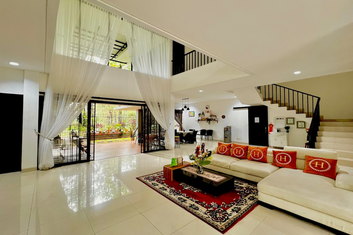 A spacious living area features a soft sectional sofa adorned with decorative cushions. Natural light fills the room through large glass doors, revealing views of the backyard. Elegant curtains drape from the ceiling, enhancing the open, welcoming ambiance.