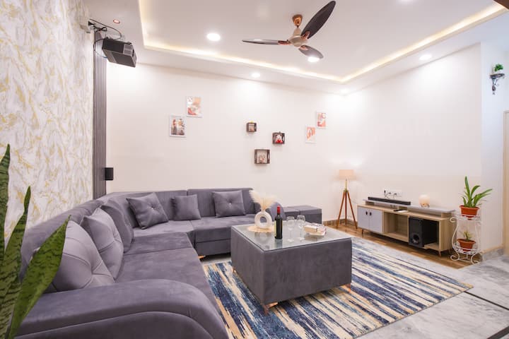 Sebule yenye starehe iliyo na mpangilio wa projekta, inayotoa Netflix, Prime, Hotstar na kadhalika. Furahia machaguo anuwai ya taa, kuanzia angavu hadi hafifu, ili kufanana na hisia zako. Imewekewa hewa safi kabisa na kupambwa kwa mimea mizuri, ikitoa mazingira ya kuburudisha.