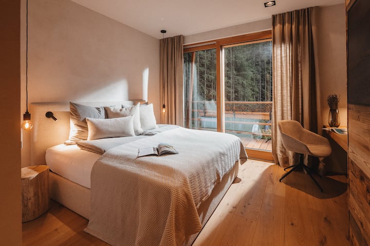 Die Balkon-Suite | Im Obergeschoss gelegen mit Zugang zum umlaufenden Balkon. Ein stiller Rückzugsort mit Blick auf den Garten, den angrenzenden Wald – und Raum für klare Gedanken.

