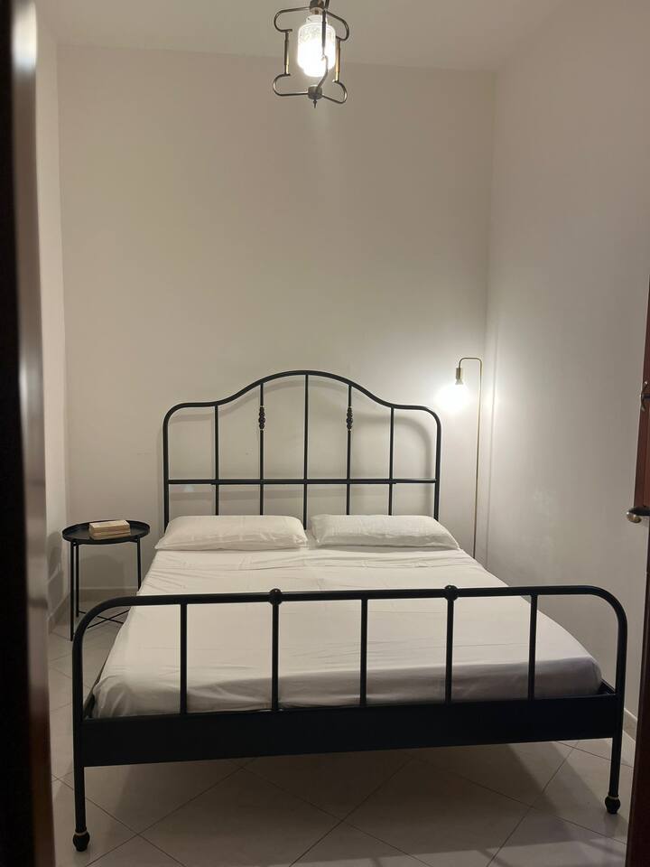 Spavaća soba s prozorom s mrežom za komarce i ventilatorom, vješalicama i ormarićima za odlaganje te odjećom iza vrata. NEMA klima-uređaja!