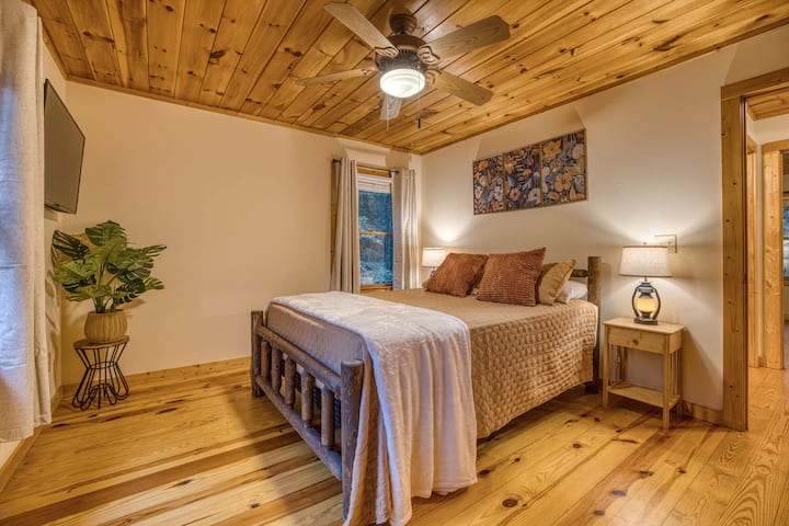 Relax in the spacious guest bedroom featuring a queen-sized luxury mattress, rustic nightstands with lamps, a large closet, Smart TV, and a cozy rocking chair. The perfect blend of comfort and charm for a restful stay!