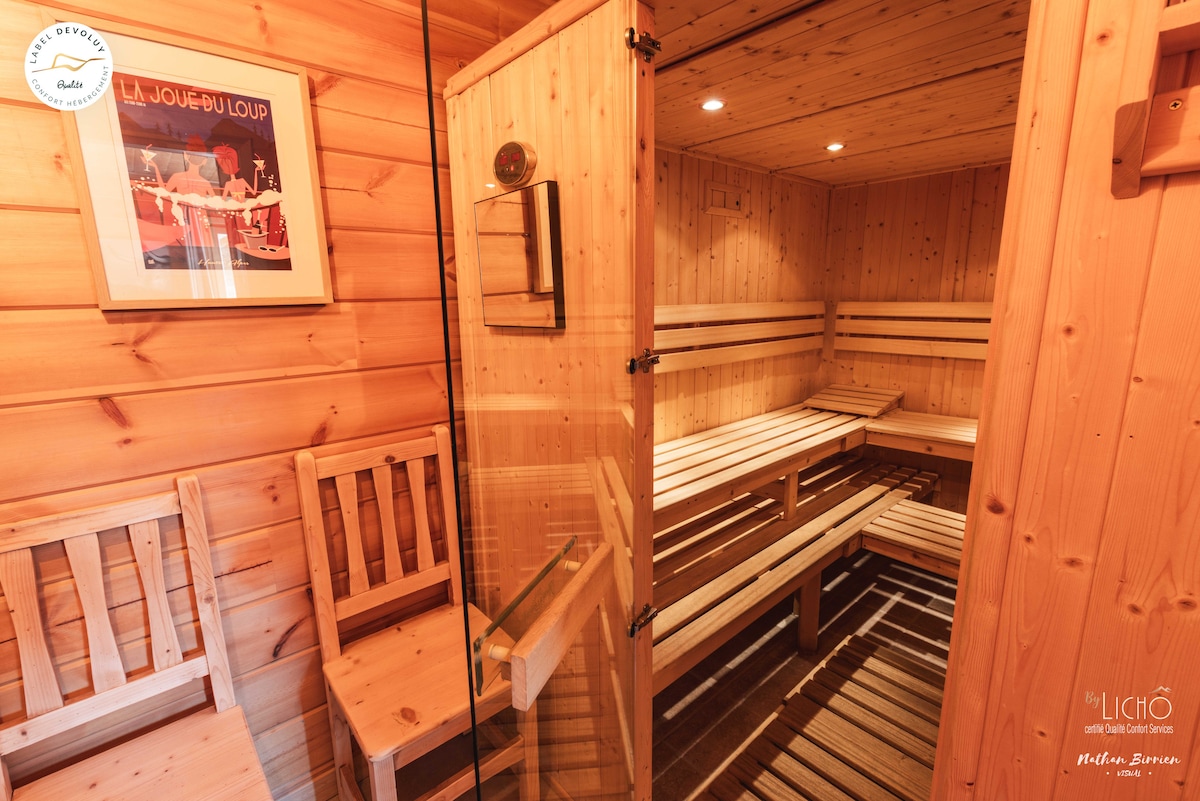 A wooden sauna is visible, featuring multiple bench seating options and wood paneling. Soft lighting creates a warm ambiance, with small recessed lights adding a gentle glow. The floor is covered in slatted wood, complementing the overall design.
