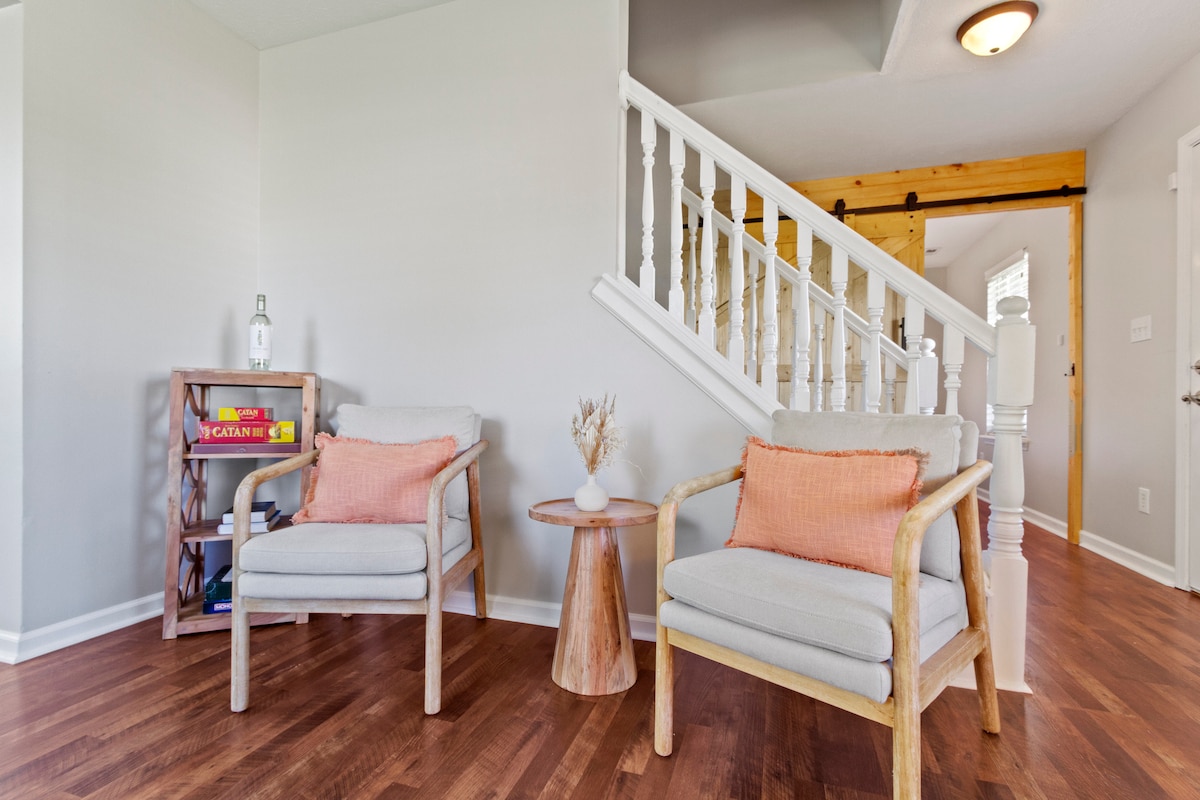 haven of style and comfort with our stunning design armchairs, featuring luxurious matching pillows, perfectly paired with an elegant designer round side table. Additionally, there is a designer shelf filled with table games and books.