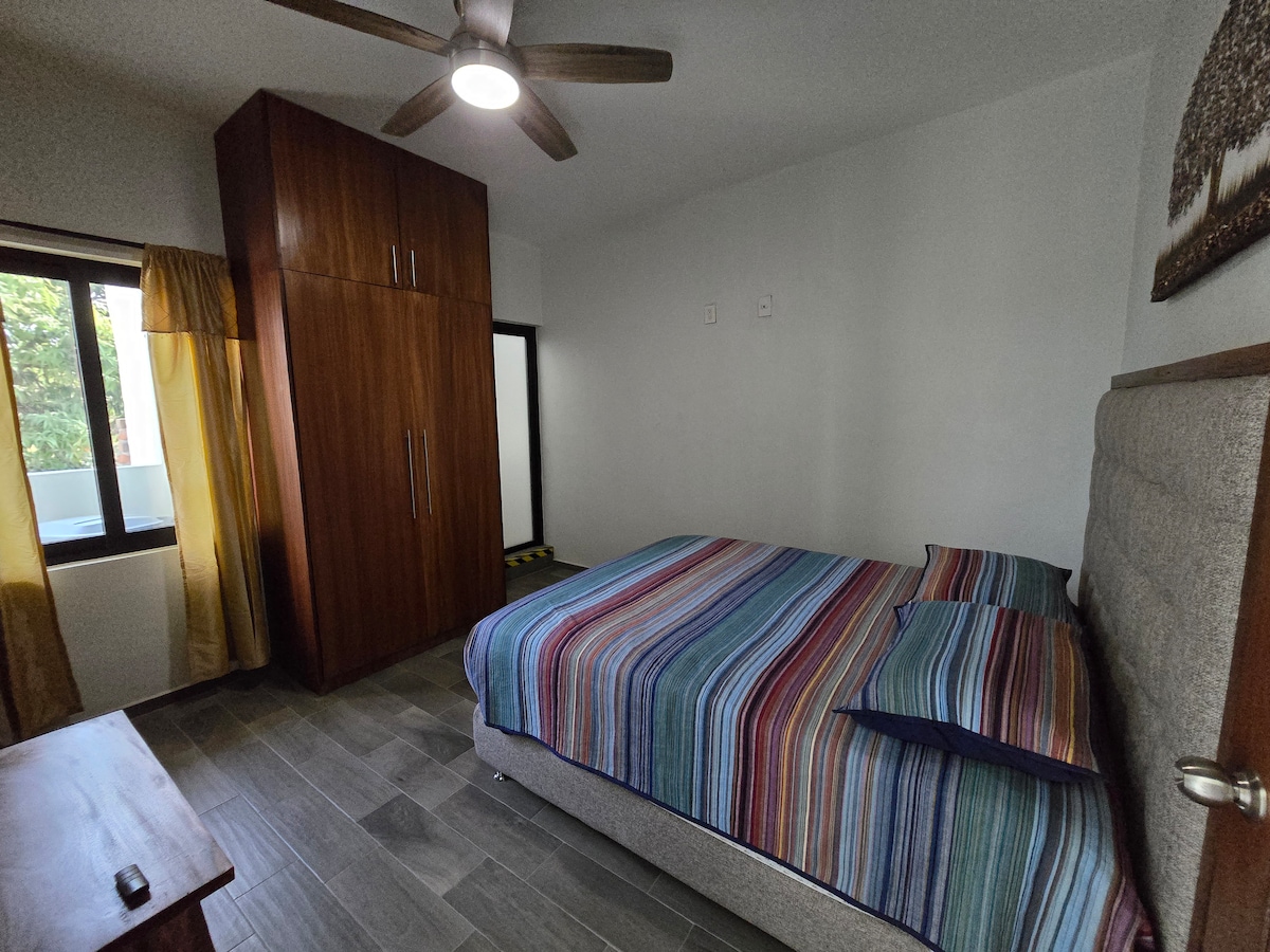 Relájate en la habitación secundaria con cama matrimonial, aire acondicionado y un ventilador refrescante. No olvides el espacioso closet con ganchos para mantener tu ropa impecable, junto a un baño privado.