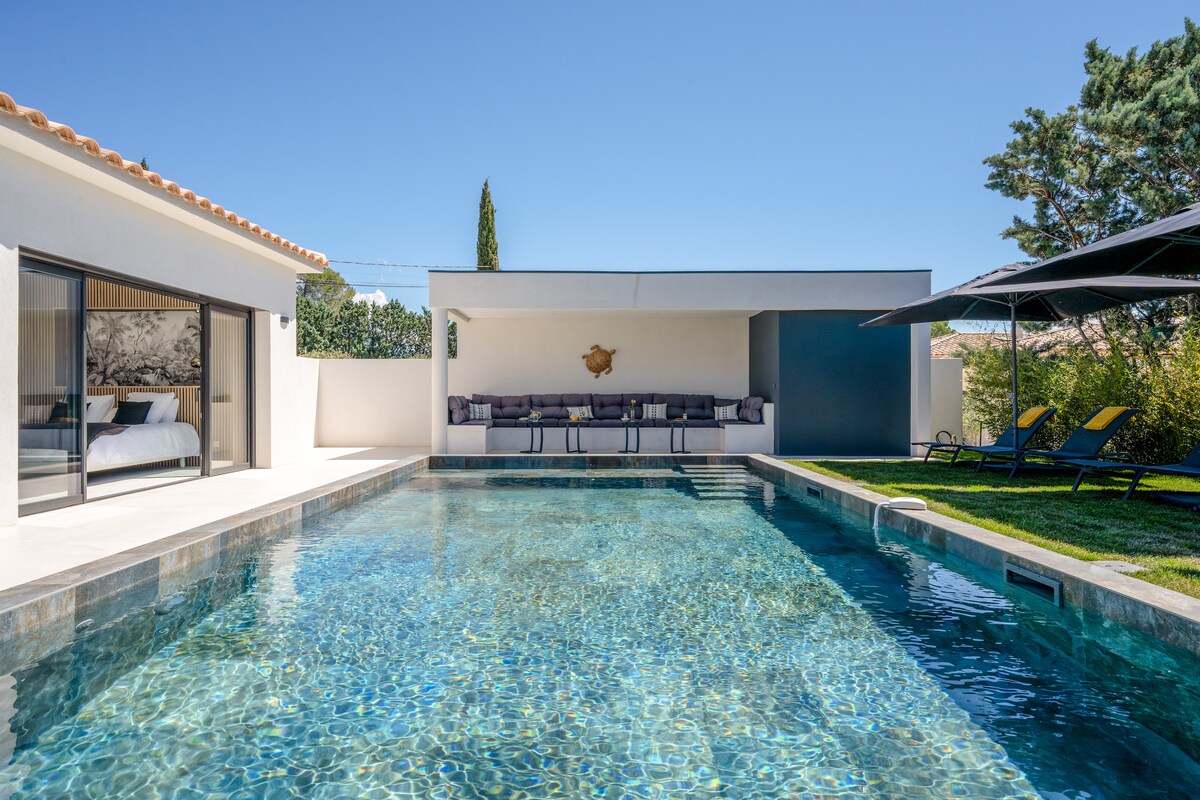 The outdoor area features a spacious salt-water pool, reflecting the bright blue sky above. A shaded lounge area is visible, offering comfortable seating for relaxation. Sun loungers are positioned nearby, inviting moments of leisure by the water's edge.