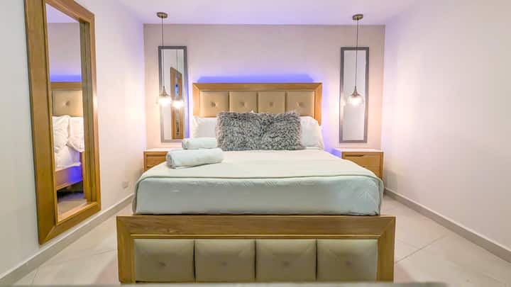 Disfruta de un descanso reparador en esta habitación espaciosa, con una cama cómoda, luces cálidas, espejos decorativos y veladores para mayor comodidad. 