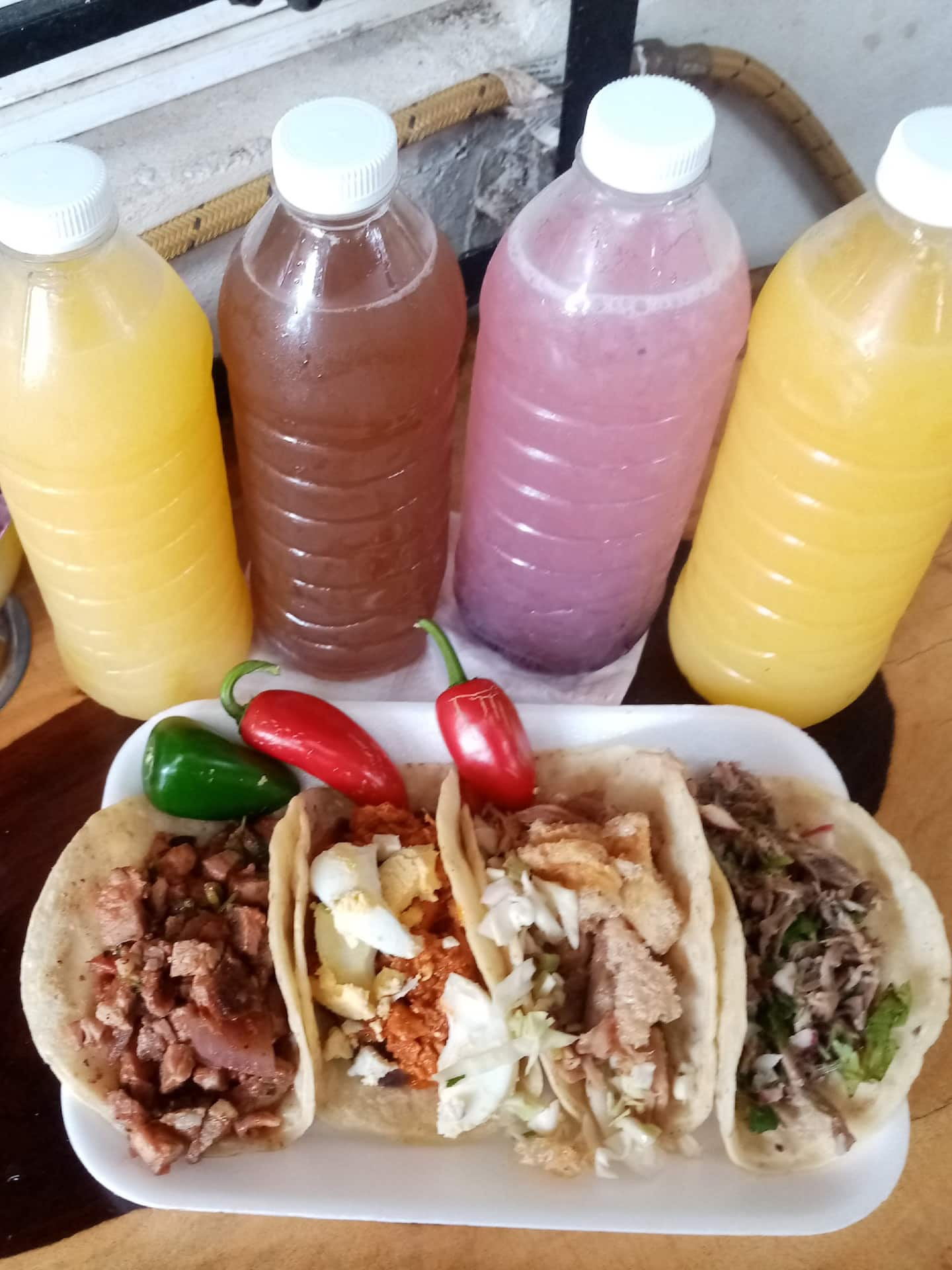 small plate with four tacos and four different colored beverages in plastic bottles