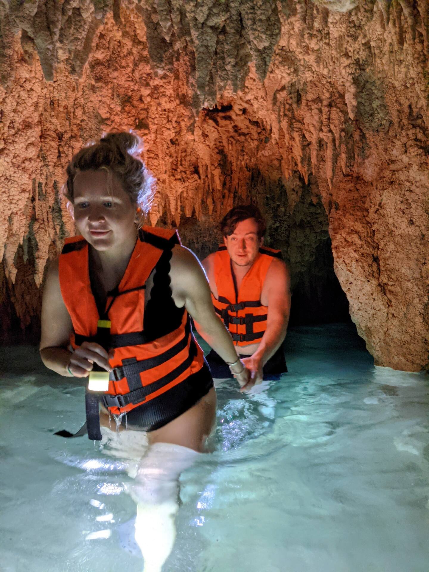 man and woman in orange life jackets walking through one of the best tulum cenotes in mexico, located underground in a cave | Cenotes Tours Tulum