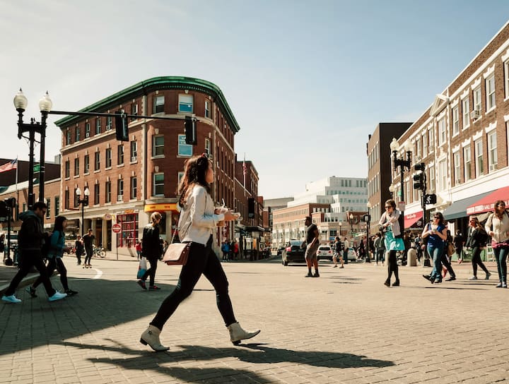 Two people walking past a heritage-style terrace house with ornate iron railings and a blue front door, on a sunny street in New South Wales.