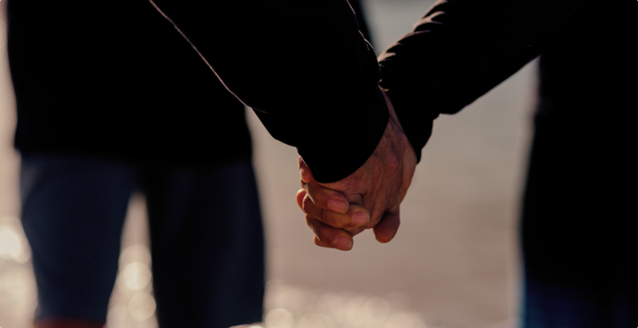 People form a circle holding hands while standing on a beach in front of the water.