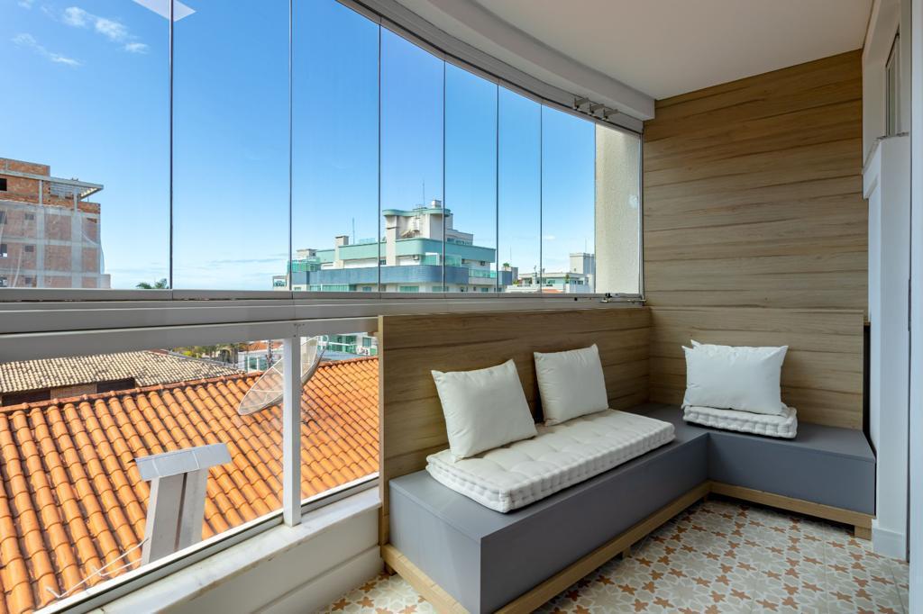 A bright, airy corner seating area features large windows with unobstructed views. Soft cushions are arranged on a built-in bench, complementing the light wooden accents and patterned floor tiles. Natural light enhances the space, creating a welcoming environment.