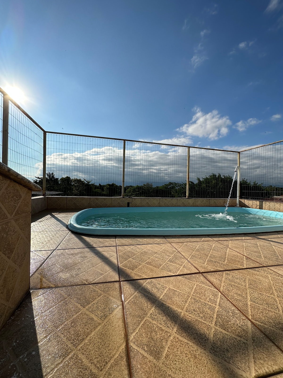 A private pool is situated on a terrace with safety fencing, surrounded by scenic views of the landscape. The water appears clear and inviting, and sunlight reflects off the surface. The pool area features textured tile flooring enhancing the tranquil atmosphere.