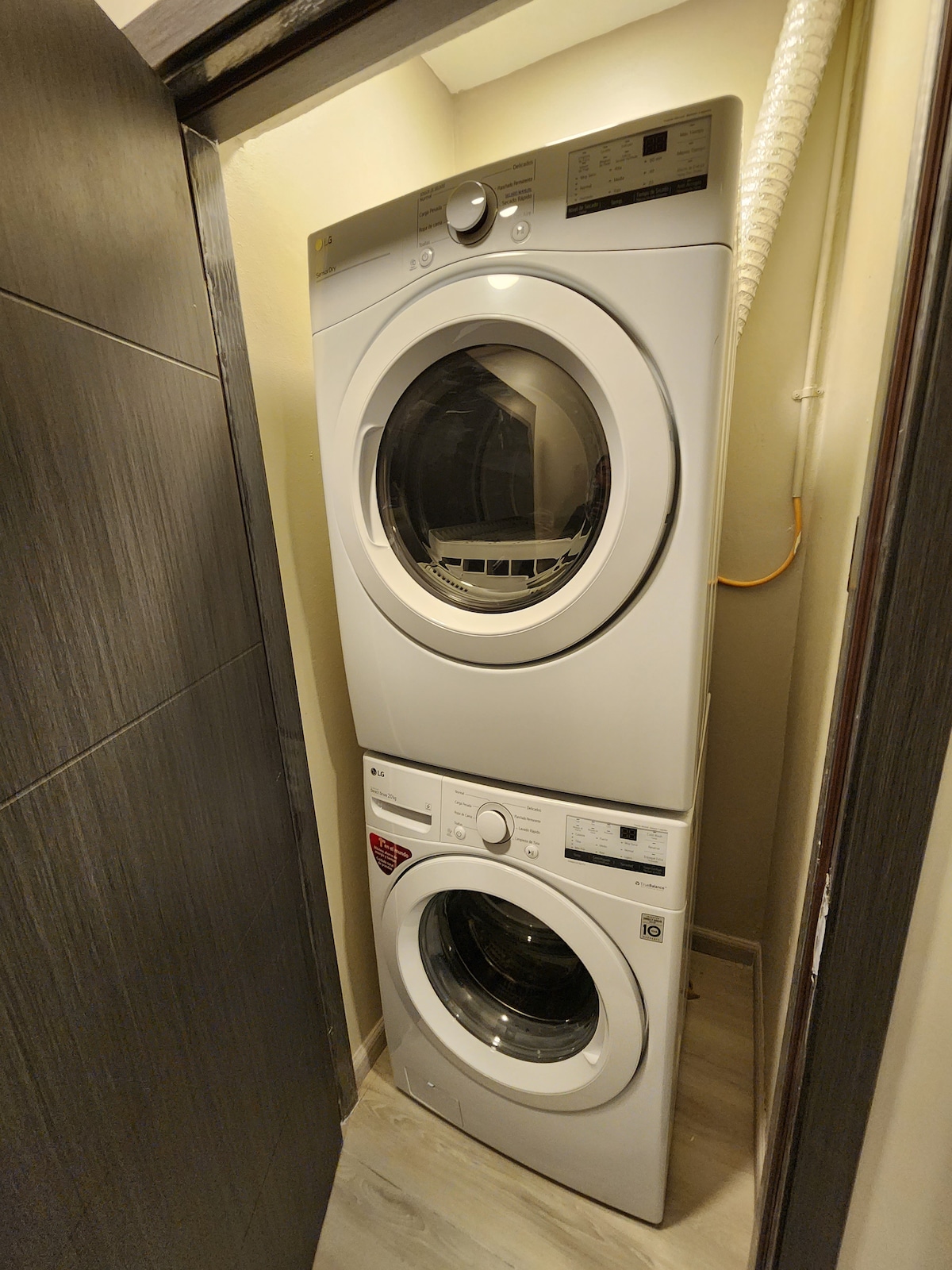 A modern stacked washer and dryer unit is positioned in a compact laundry area. The units are white, featuring circular doors and a sleek design, with a light-colored floor enhancing the brightness of the space.